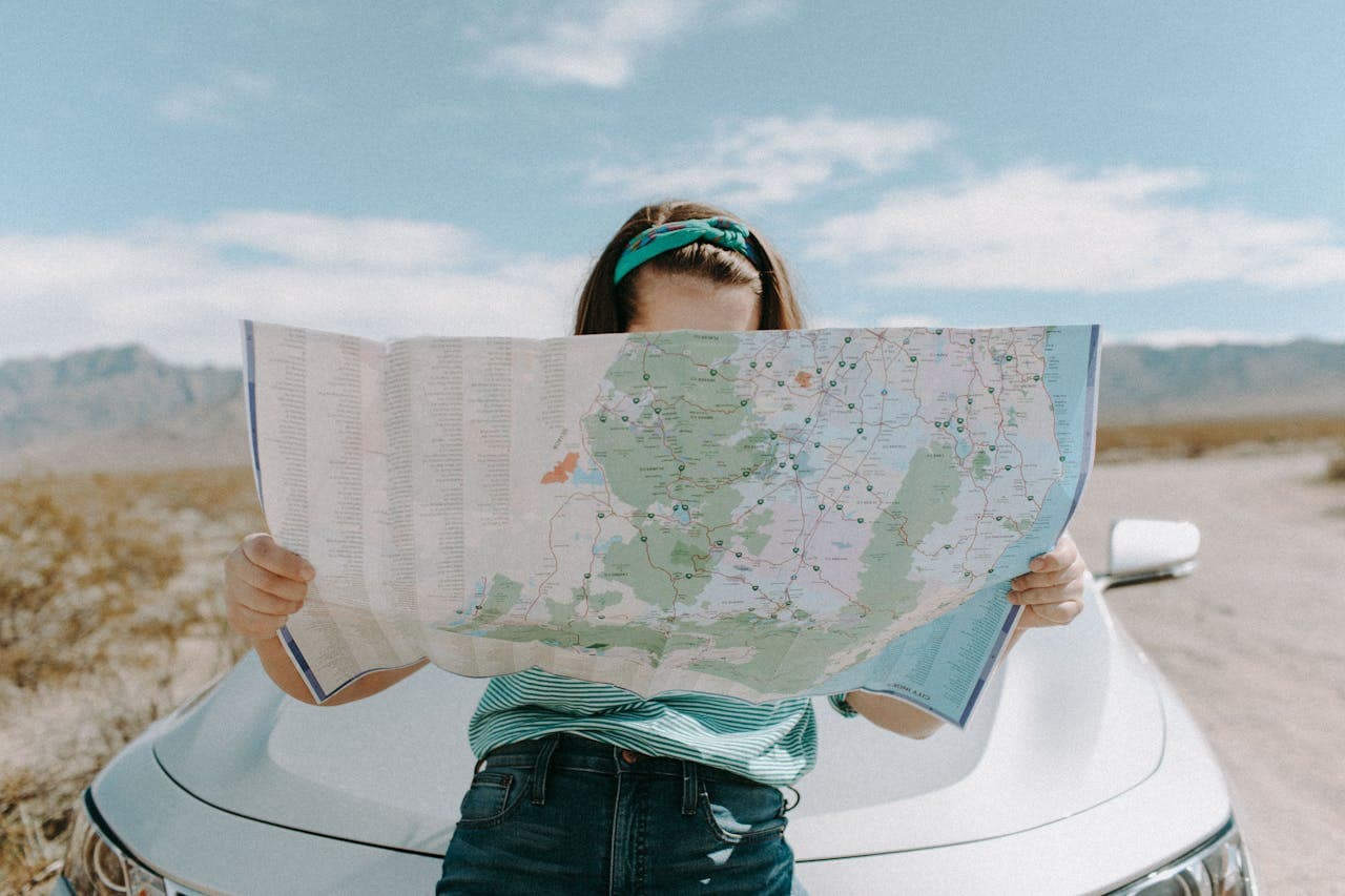 Uma pessoa procura uma rota em um mapa enquanto está encostada em um carro em uma estrada de terra, em um lugar deserto.